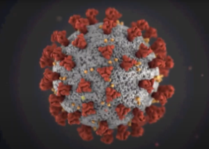 A 3D rendering of the COVID-19 virus, depicted as a gray spherical structure covered with red spike proteins and small yellow particles, set against a dark background.